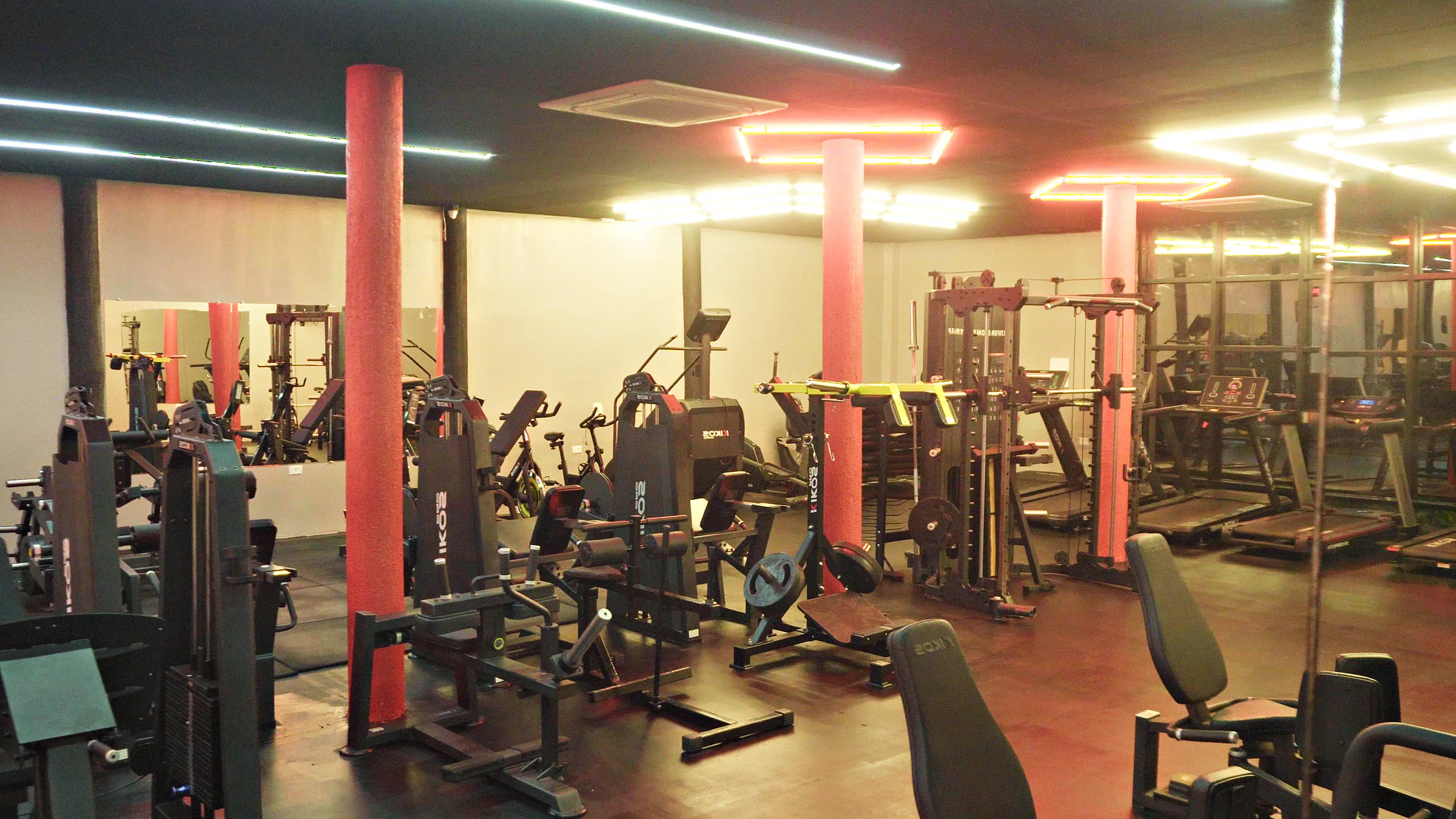 Andar de cima, com LED vermelho e branco no teto, pilares vermelhos e as máquinas Kikos