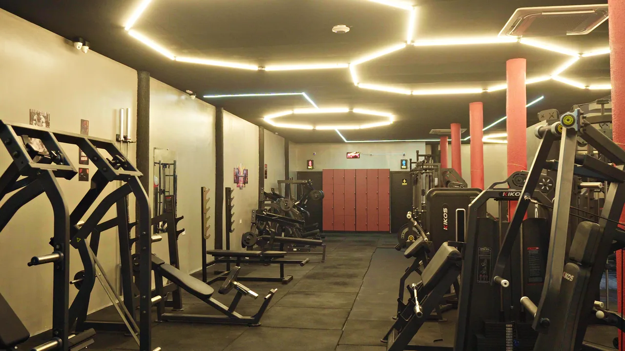 Térreo da academia com luzes de LED em hexágono no teto e os armários vermelhos ao fundo